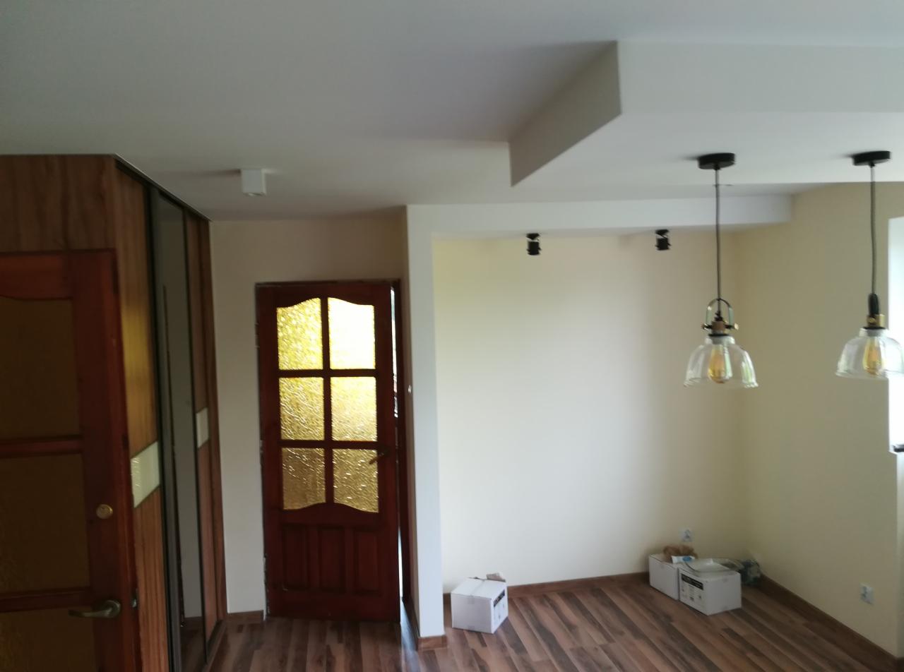 Pomalowane na jasno ściany pokoju z drewnianą podłogą, widoczne dwie wiszące lampy w stylu retro, drewniane drzwi z szybkami oraz częściowo widoczna szafa przesuwna.