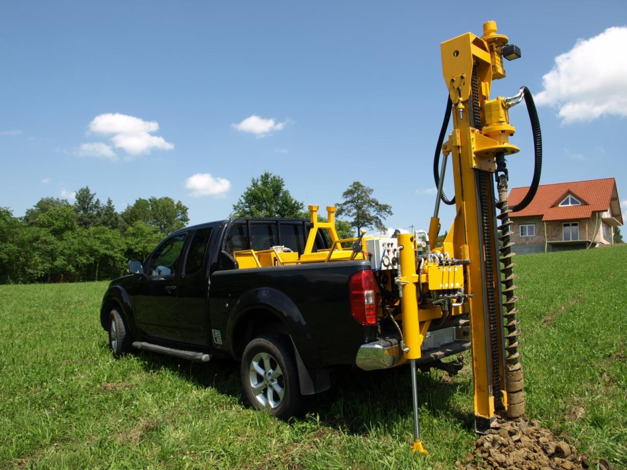 Wiertnica zamontowana na pickupie w Chorowicach, wykonująca odwiert w gruncie na tle zielonej łąki i domu jednorodzinnego.