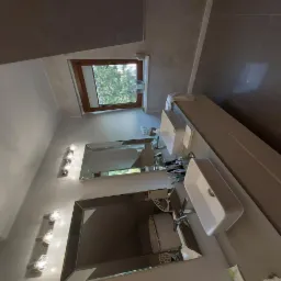 Wykończona łazienka na poddaszu z dwoma umywalkami, lustrami z ozdobnymi ramami i oknem dachowym z widokiem na zieleń. Ściany wykończone w szarościach.