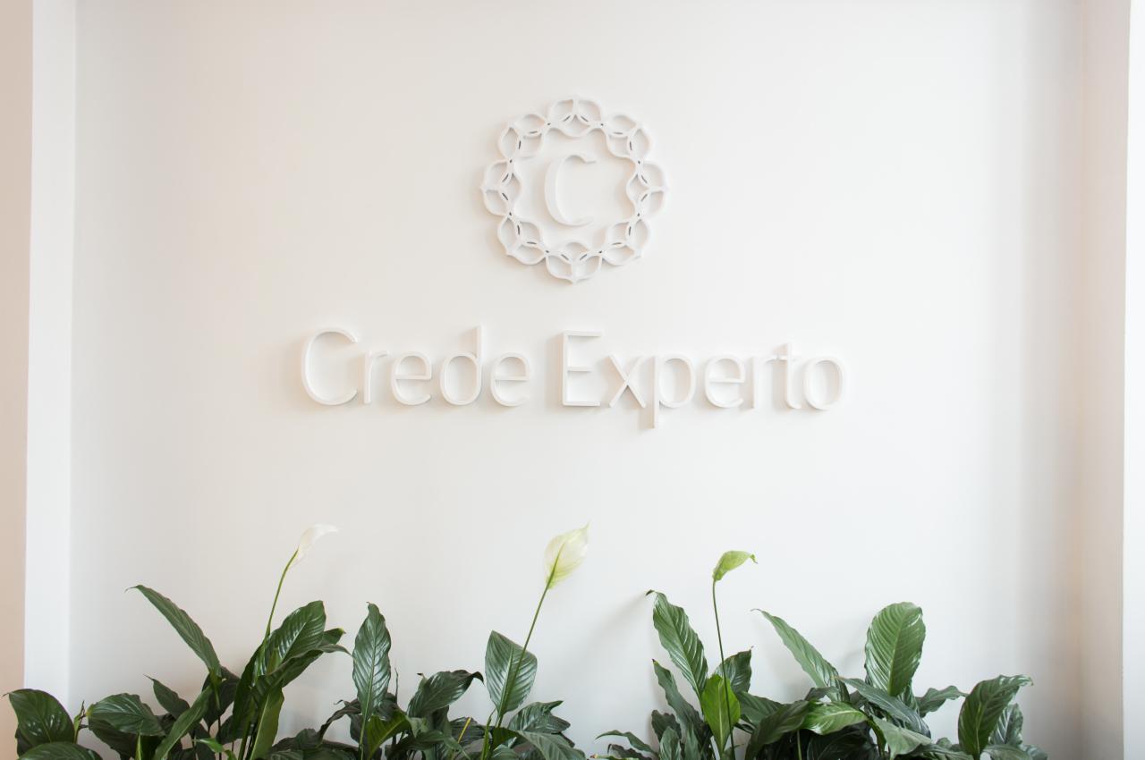 Minimalistyczne biuro z białym logo 'Crede Experto' na ścianie, ozdobione roślinami doniczkowymi