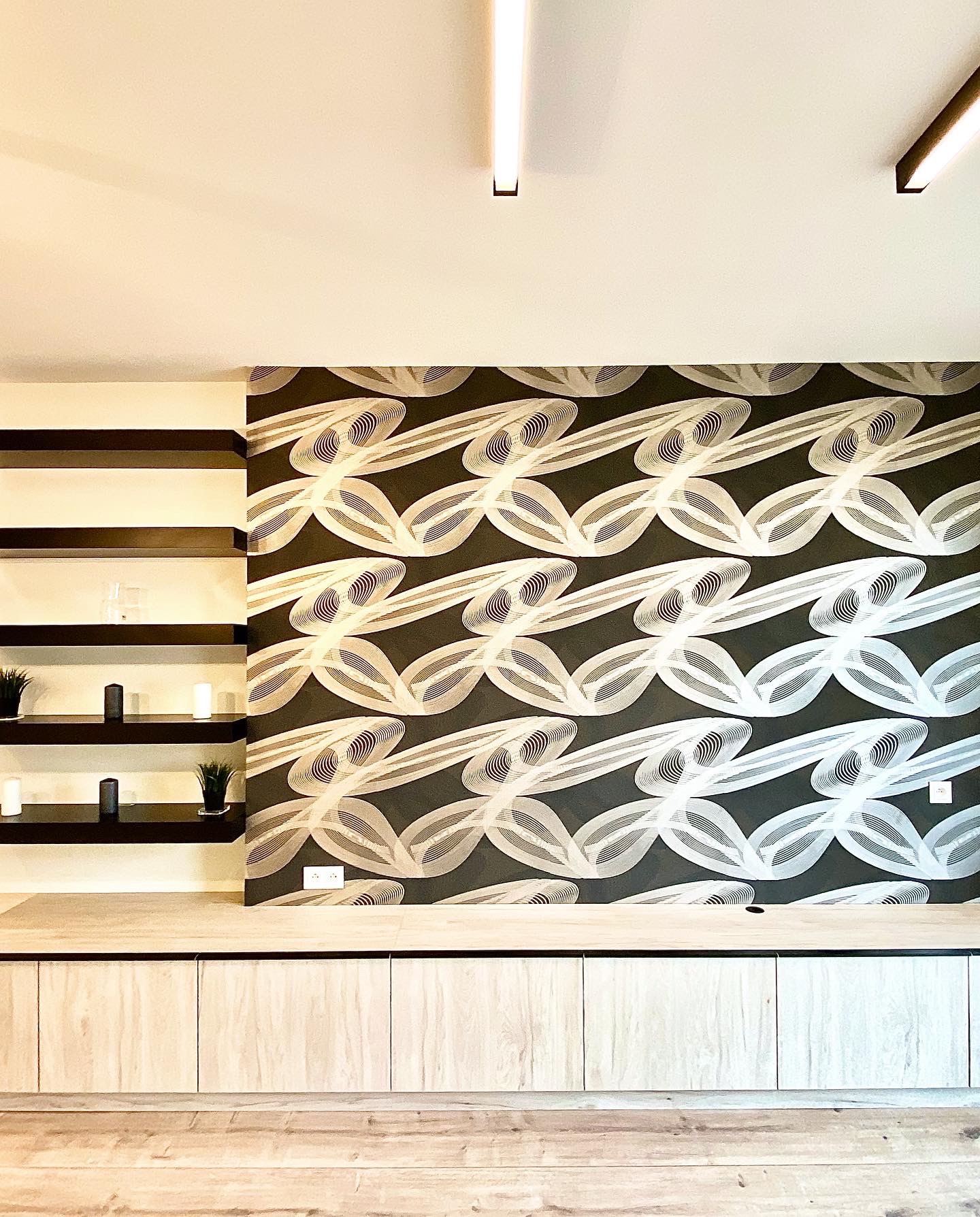 Nowoczesne wnętrze z tapetą w geometryczne wzory, drewnianą podłogą i półkami z dekoracjami, oświetlone listwami LED.