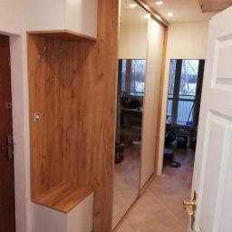 P.P.H Mag - Przedpokój z zabudową: drewnopodobny panel z wieszakami i siedziskiem, obok szafa przesuwna z lustrami, widok z otwartych drzwi.