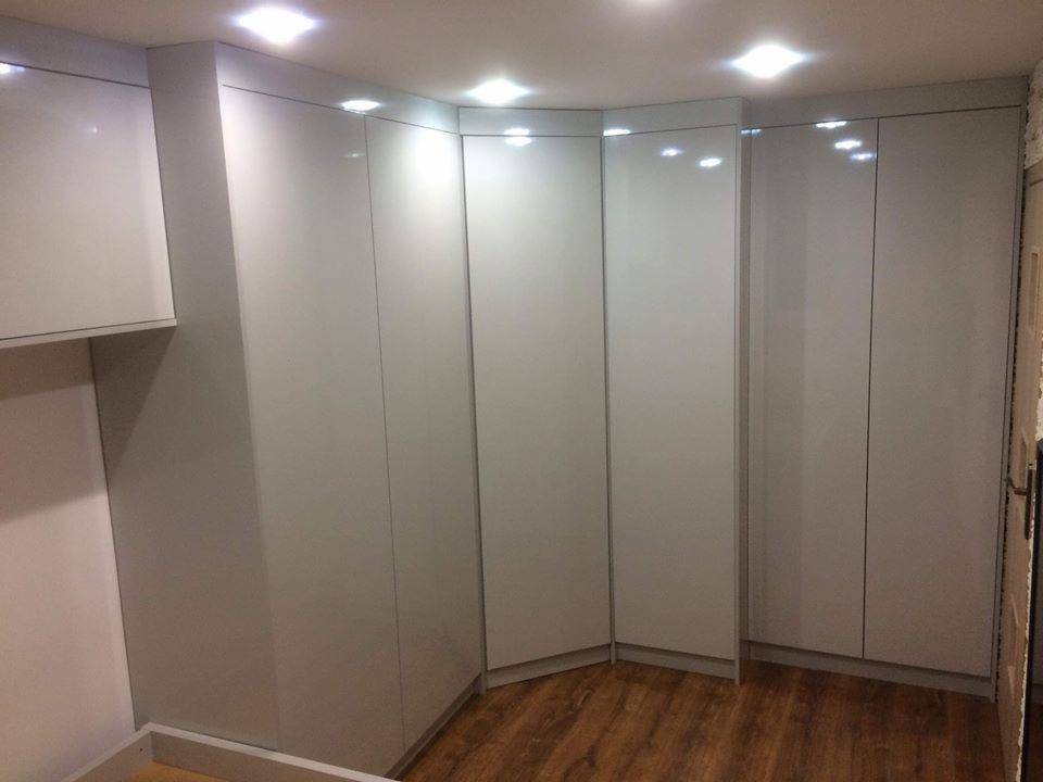 Zabudowa narożna z białych, lakierowanych szaf z delikatnymi uchwytami, dopasowana do niskiego sufitu, z widoczną drewnopodobną podłogą.