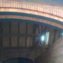 Wzmocnienie łuku ceglanego nad przejazdem za pomocą metalowej belki mocowanej na śruby.