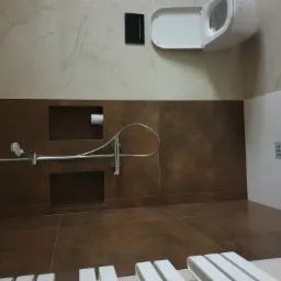 Nowoczesna łazienka z brązowymi i beżowymi płytkami, wiszącą toaletą i chromowaną armaturą prysznicową.