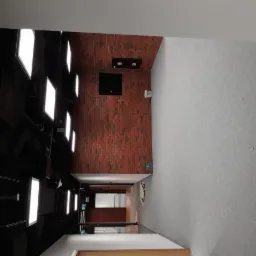 Korytarz biurowy po remoncie z ceglaną ścianą, szarą wykładziną i nowoczesnym oświetleniem sufitowym.