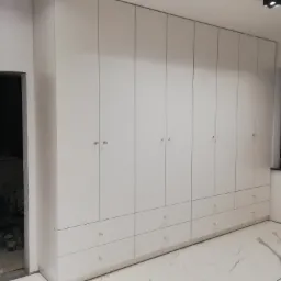 Biała, wysoka zabudowa szafowa z kryształowymi gałkami na tle marmurowej podłogi, widok na wnętrze remontowanego pomieszczenia.