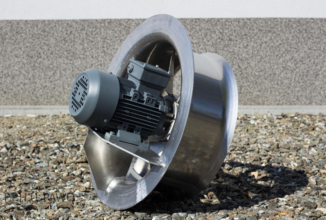 Nowoczesny, metalowy wentylator przemysłowy z szarym silnikiem, ustawiony na żwirowym podłożu przed szarą ścianą budynku.