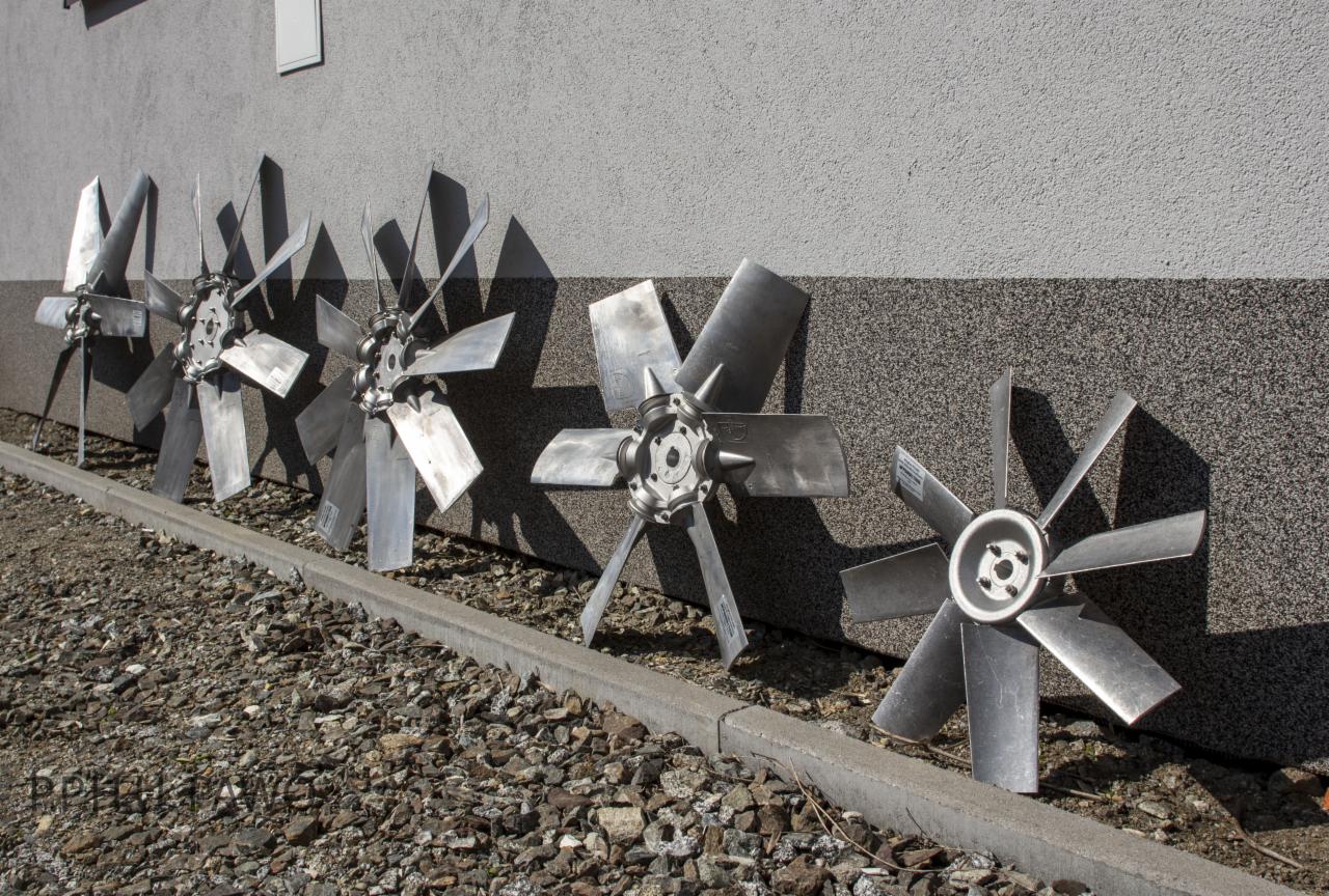 Rząd metalowych wentylatorów przemysłowych opartych o szarą ścianę z drobnym kamyczkiem u podstawy.