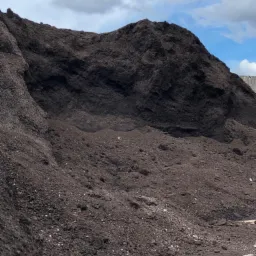 Góra usypanej ziemi z widocznymi grudkami i kamieniami, na tle błękitnego nieba z chmurami.