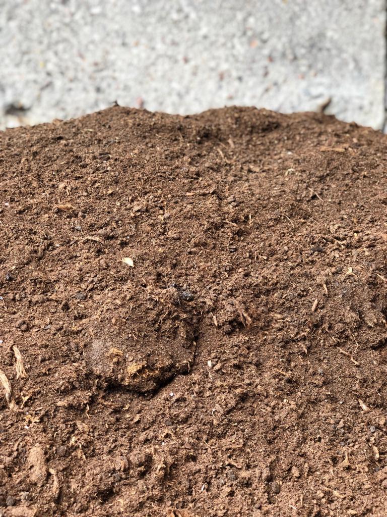 Kupa ciemnej ziemi z widocznymi fragmentami korzeni i grudkami, na tle betonowej powierzchni.