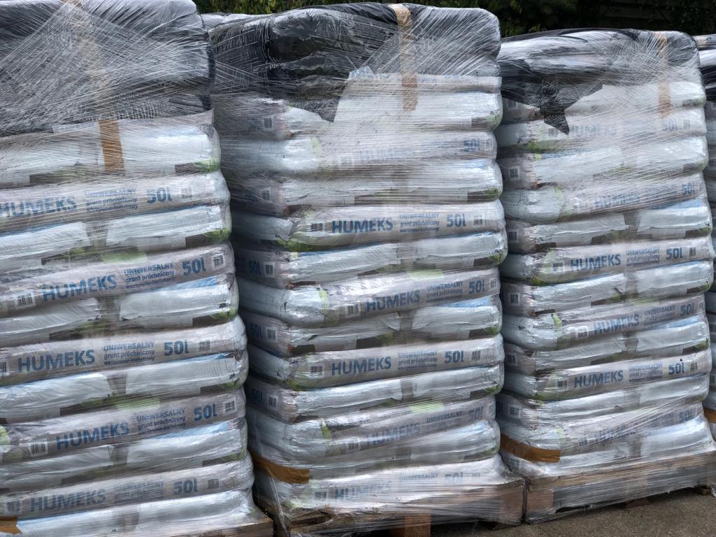 Palety z workami ziemi uniwersalnej HUMEKS 50l, owinięte folią stretch, składowane na zewnątrz.