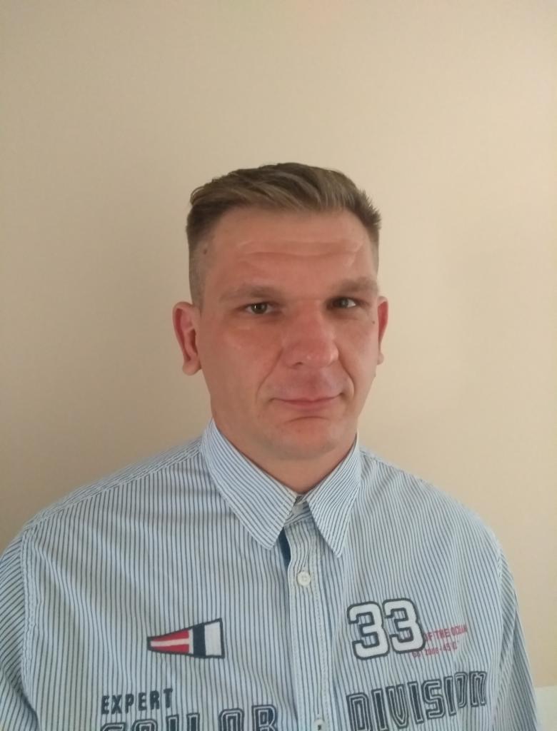 Portret mężczyzny w koszuli w paski, Lublin. Widoczny fragment koszuli z napisem '33 DIVISION'. Neutralne tło, oświetlenie naturalne, brak elementów rozpraszających.