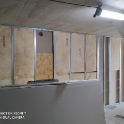 Montaż ścian działowych: metalowy szkielet z izolacją Isover i częściowo zamontowaną płytą karton-gips, widoczne niedokończone łączenia płyt.