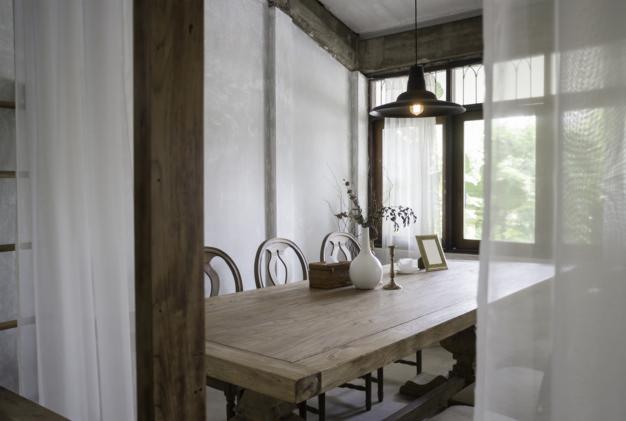 Jasne wnętrze jadalni z drewnianym stołem, krzesłami o ażurowych oparciach i minimalistycznymi dekoracjami, wisząca lampa z żarówką Edisona