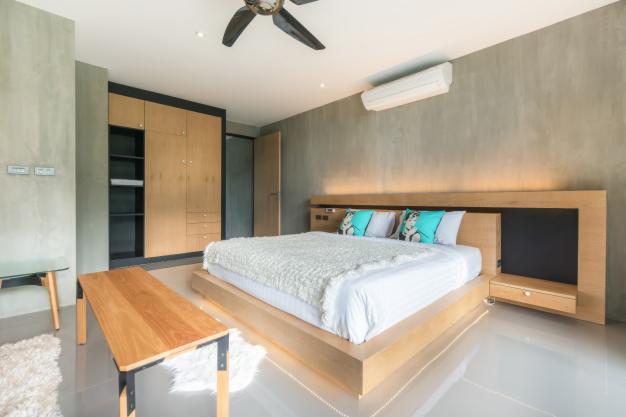 Nowoczesna sypialnia z łóżkiem na podwyższeniu, drewnianą szafą w zabudowie i szarą ścianą z klimatyzatorem.