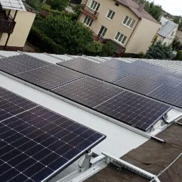 Panel fotowoltaiczny zamontowany na dachu budynku mieszkalnego, widoczne mocowania i część instalacji odgromowej.