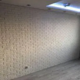 Ściana z białej cegły dekoracyjnej w nowym pomieszczeniu z szarymi panelami podłogowymi i oświetleniem sufitowym w kształcie kwadratu.