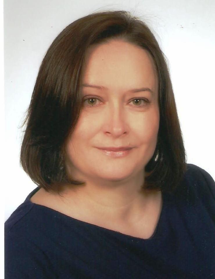 Portret kobiety z brązowymi włosami i zielonymi oczami, uśmiechająca się delikatnie, na jasnym tle.