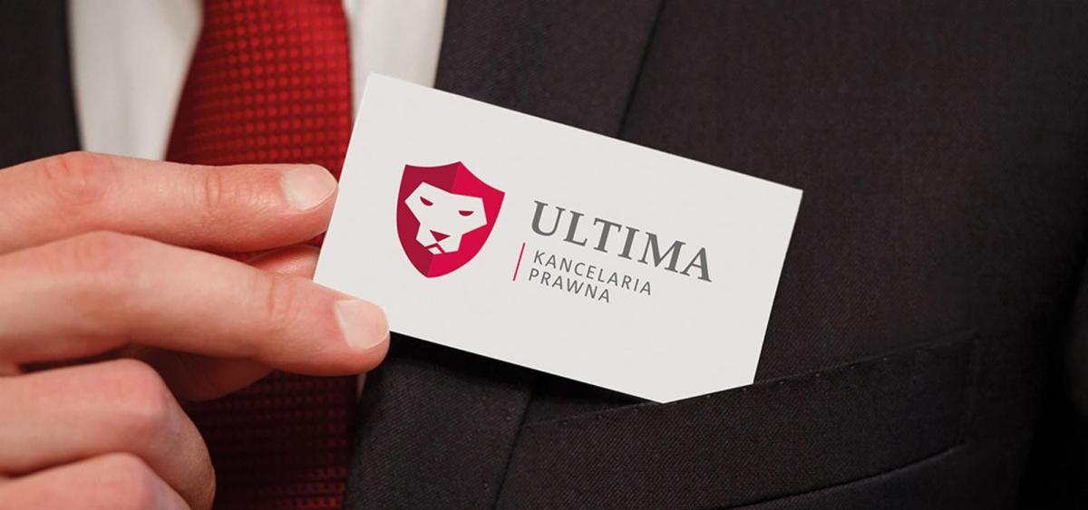 Wizytówka kancelarii prawnej Ultima z logo lwa w tarczy, włożona do kieszeni marynarki, widoczny fragment czerwonego krawata w tle.