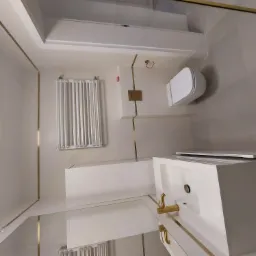 Nowoczesna łazienka w bieli z akcentami złotych listew: umywalka z baterią, toaleta, grzejnik żeberkowy, oświetlenie w tle.