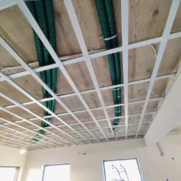 Konstrukcja sufitu podwieszanego z widocznymi zielonymi rurami instalacyjnymi przymocowanymi do stropu za pomocą metalowych obejm.