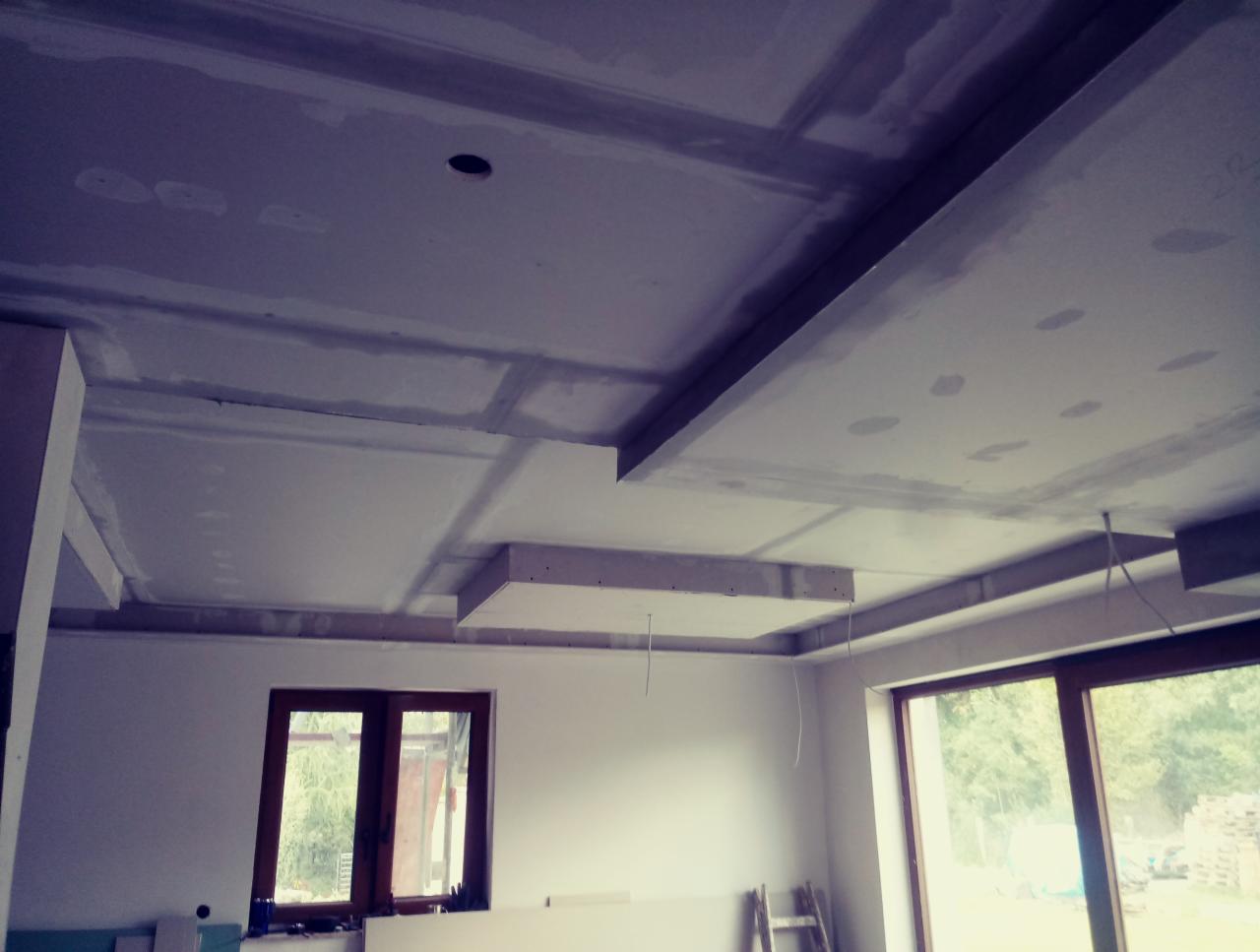 Sufit podwieszany z płyt gipsowo-kartonowych w trakcie montażu, widoczne łączenia i niedoskonałości, okna w tle, drabina oparta o ścianę.