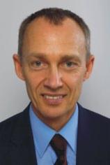 Portret mężczyzny w garniturze, uśmiechniętego, z Gdyni, z widocznymi zmarszczkami mimicznymi wokół oczu.