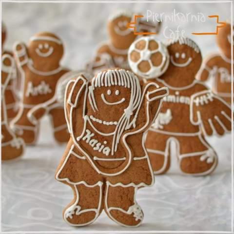 Dekoracyjne pierniczki w kształcie ludzików i piłki, zdobione białym lukrem z imionami, na jasnym tle.