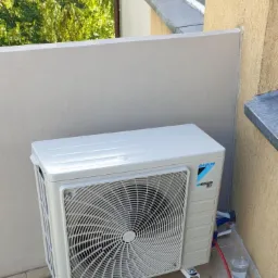 Biała jednostka zewnętrzna klimatyzacji Daikin na balkonie, widoczne narzędzia i szklanka z wodą po instalacji.