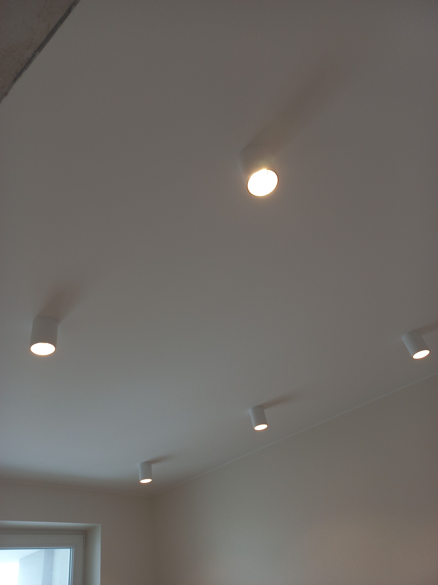 Biały sufit z zamontowanymi cylindrycznymi lampami punktowymi LED, rozmieszczonymi w nieregularny sposób, oświetlającymi wnętrze.
