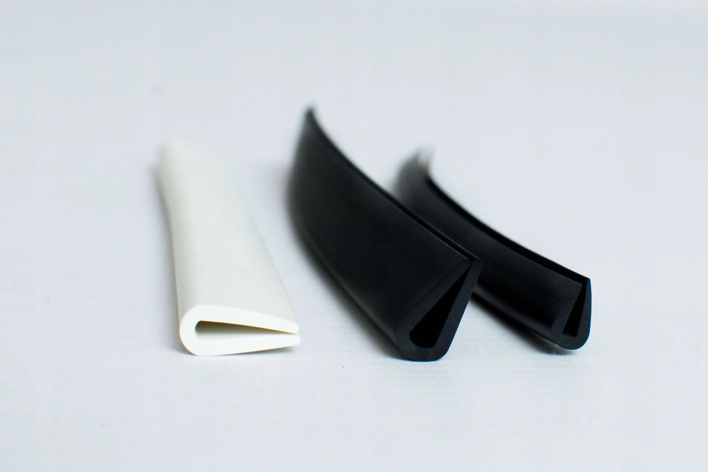 Profil uszczelniający w kształcie litery U: biały i dwa czarne, leżące na białym tle, prezentujące przekrój poprzeczny.