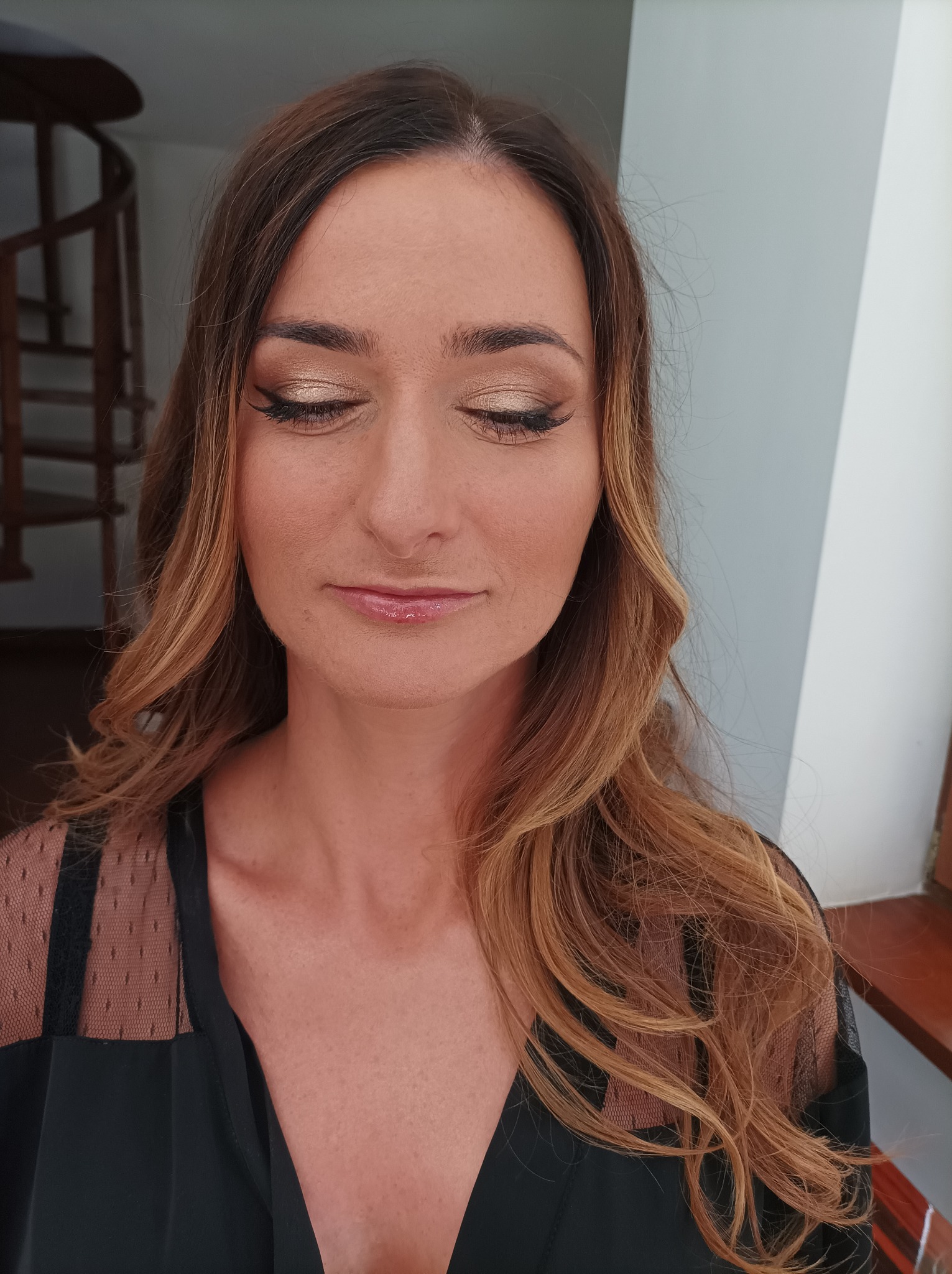 Portret kobiety z zamkniętymi oczami, prezentującej delikatny, złoty cień na powiekach, podkreślony czarną kreską i wydłużonymi rzęsami, z błyszczącymi ustami i włosami w odcieniach brązu i blondu.