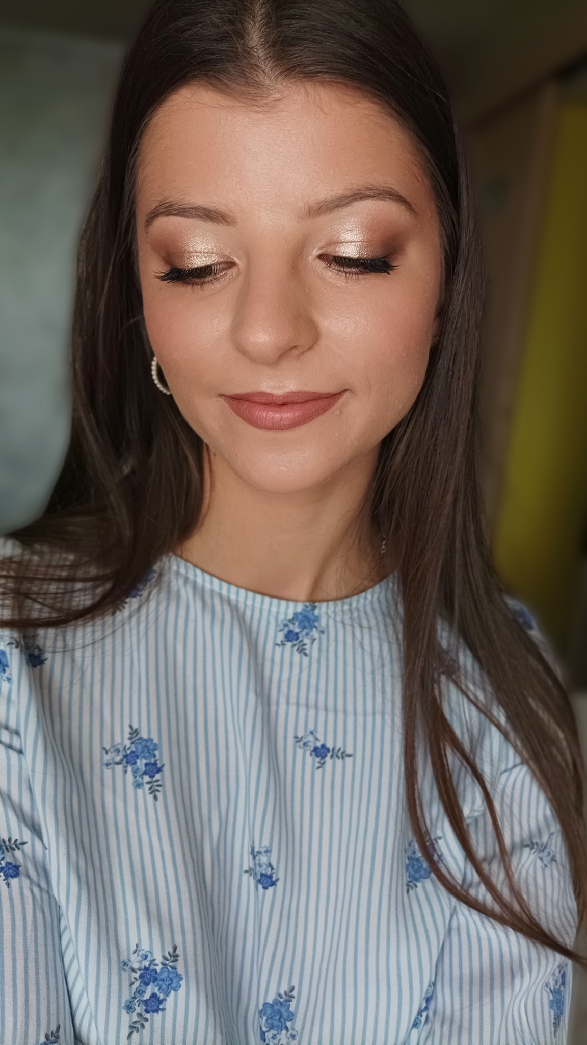 Portret kobiety z zamkniętymi oczami, prezentującej delikatny, rozświetlony makijaż oka w odcieniach złota i brązu, z widocznymi sztucznymi rzęsami i subtelną pomadką w kolorze nude, ubrana...