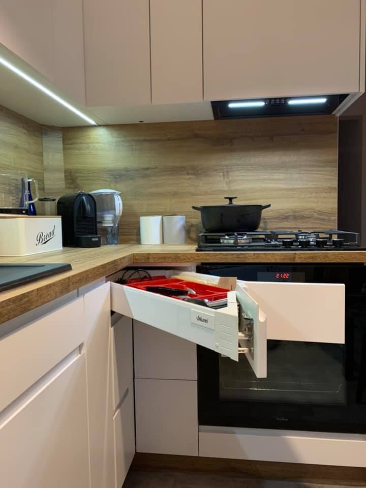 Nowoczesna kuchnia z białymi frontami, drewnianym blatem i otwartą szufladą narożną z organizerem na sztućce firmy Blum.