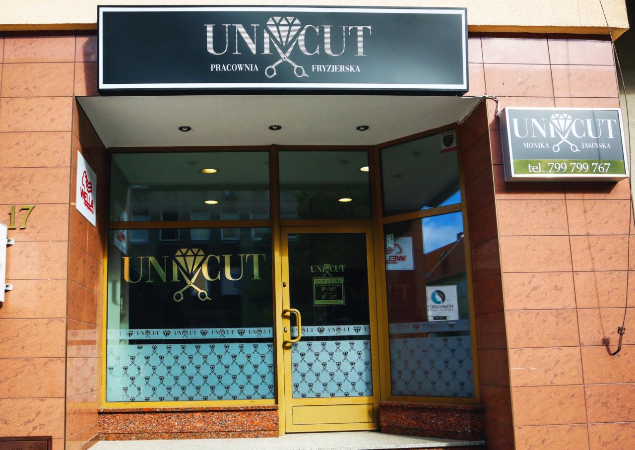 Wejście do salonu z szyldem 'Unicut' z grafiką diamentu i nożyczek, okna z dekoracyjnym wzorem nożyczek i diamentów, tabliczka z numerem telefonu.