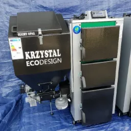 Nowoczesny kocioł na paliwo stałe marki Krzystał ECODESIGN z zasobnikiem na suchy opał, ustawiony na niebieskiej plandece.