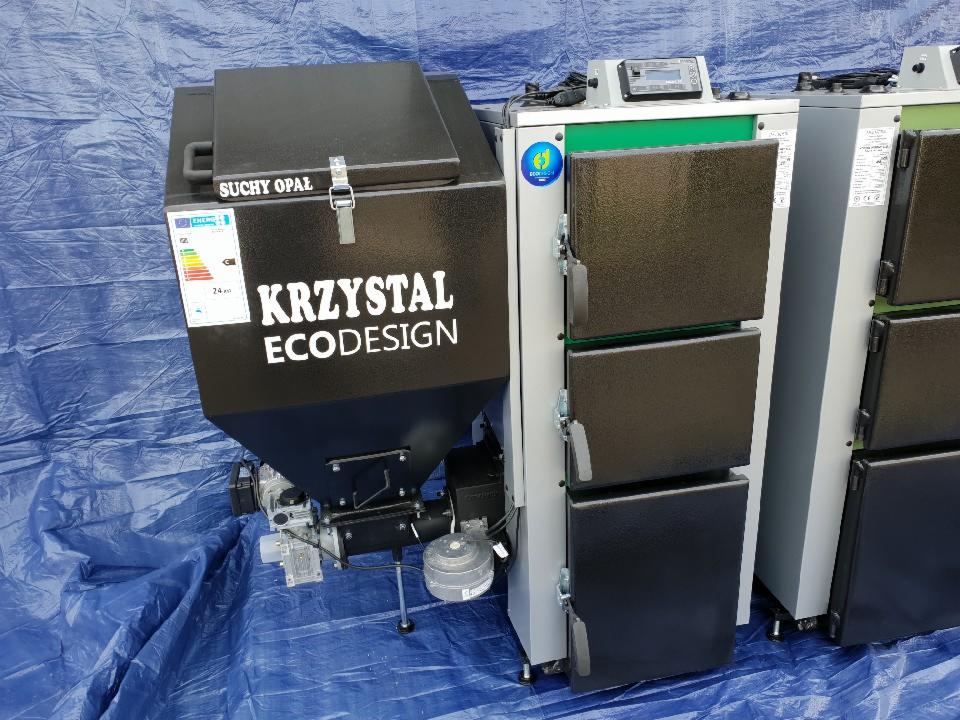 Nowoczesny kocioł na paliwo stałe marki Krzystał ECODESIGN z zasobnikiem na suchy opał, ustawiony na niebieskiej plandece.