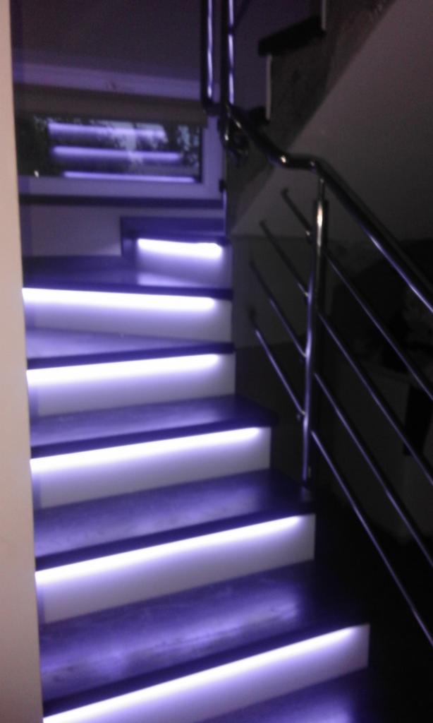 Schody z podświetleniem LED w kolorze fioletowym, z metalową balustradą, widok z dołu.