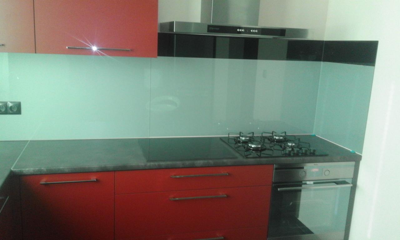 Nowoczesna kuchnia z czerwonymi szafkami, szklanym panelem nad blatem i czarnym blatem.