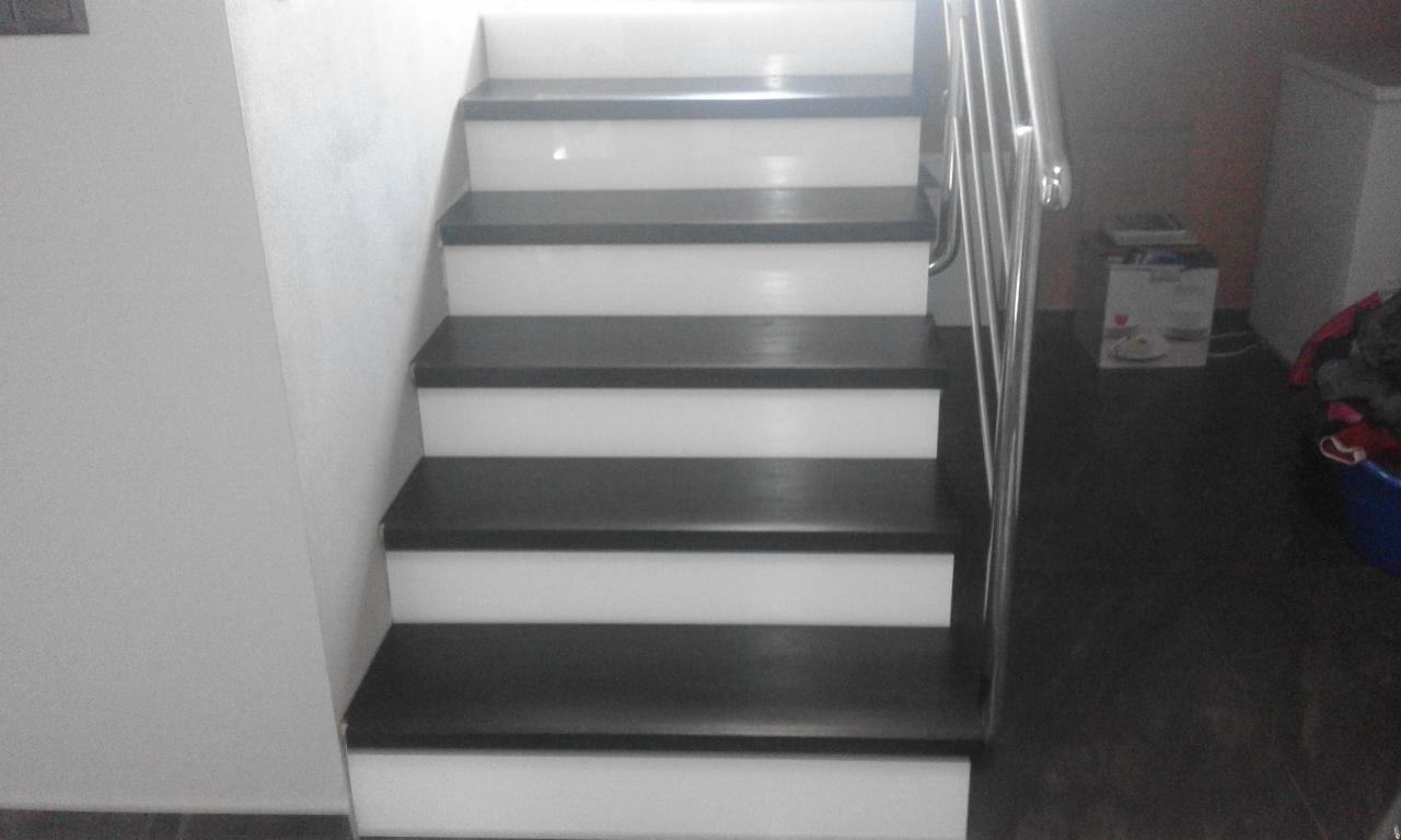 Odnowione schody z ciemnymi stopniami i białymi podstopnicami, widoczne metalowe poręcze i fragment ściany.