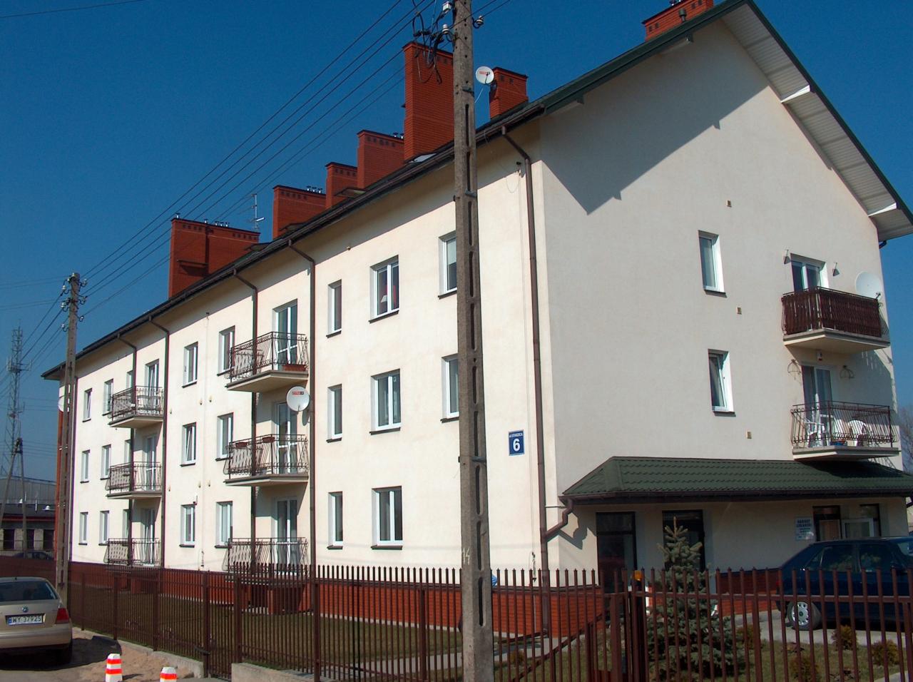 Budynek mieszkalny z balkonami i instalacją odgromową na dachu, widoczny słup elektryczny z przewodami.