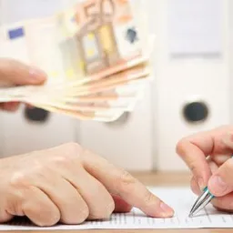 Podpis dokumentu długopisem, w tle ręka wręczająca plik banknotów euro. Białe segregatory w tle. Umowa kredytowa lub pożyczka.