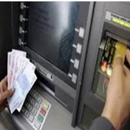 Osoba wkłada kartę do bankomatu, trzymając w drugiej ręce plik banknotów euro.