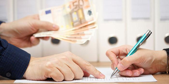 Podpis dokumentu długopisem, w tle ręka wręczająca plik banknotów euro. Białe segregatory w tle. Umowa kredytowa lub pożyczka.