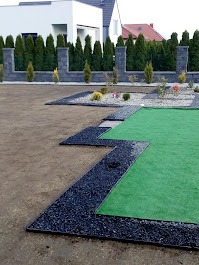 Nowoczesny ogród w trakcie tworzenia: czarny kamień oddziela trawnik od rabat, w tle żywopłot z tuj i dom. Widoczny etap prac.