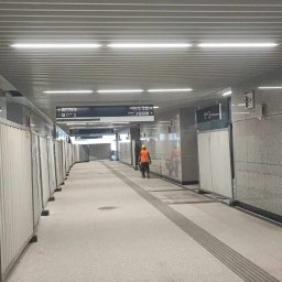 Usługi Kamieniarskie Bartłomiej Lisak - Wnętrze przejścia podziemnego w trakcie wykańczania, ściany wyłożone płytami z kamienia naturalnego, widoczne tymczasowe bariery ochronne i pracownik w stroju roboczym.