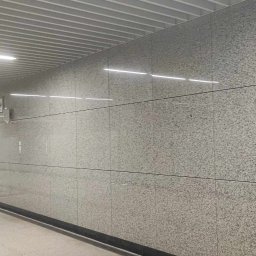 Usługi Kamieniarskie Bartłomiej Lisak - Korytarz w trakcie wykańczania z wyłożonymi płytami z szarego kamienia i pracownikiem budowlanym w oddali