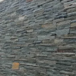 Elewacja budynku wykończona szarozielonym kamieniem łupanym ułożonym w poziome pasy, widoczne mocowanie do betonowej konstrukcji powyżej.