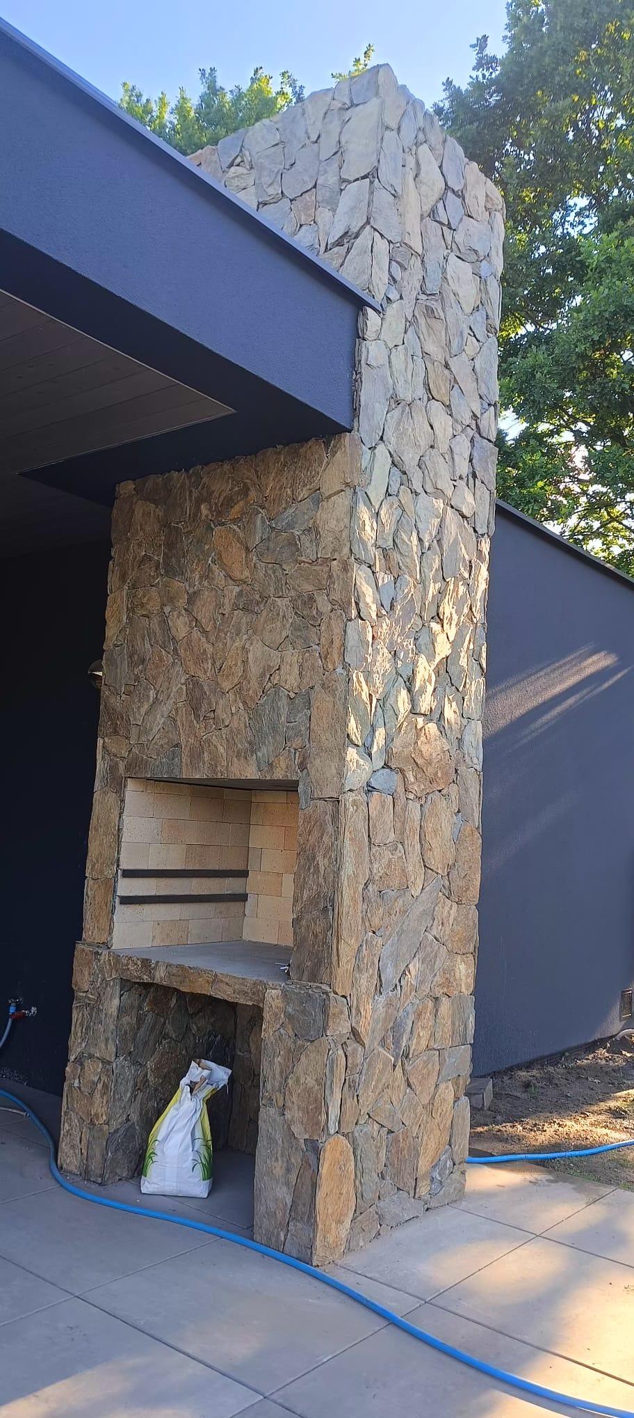 Kamienny grill ogrodowy w Szydłowcu, z paleniskiem wyłożonym cegłami i półką na akcesoria, wykonany z nieregularnych kamieni w odcieniach brązu i szarości.